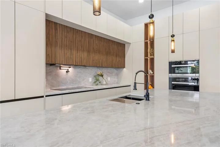Kitchen featuring a large light-toned stone countertop island with an undermount sink and black gooseneck faucet