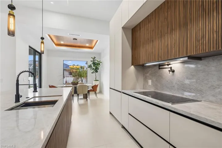 Contemporary kitchen featuring integrated appliances, light wood-finish cabinetry, a stone countertop with a waterfall edge, and a single-basin sink with a matte black pull-down faucet