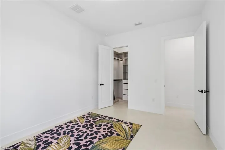 Bright white room featuring large format tile flooring, white baseboards, and a built-in closet system with shelving and drawer storage