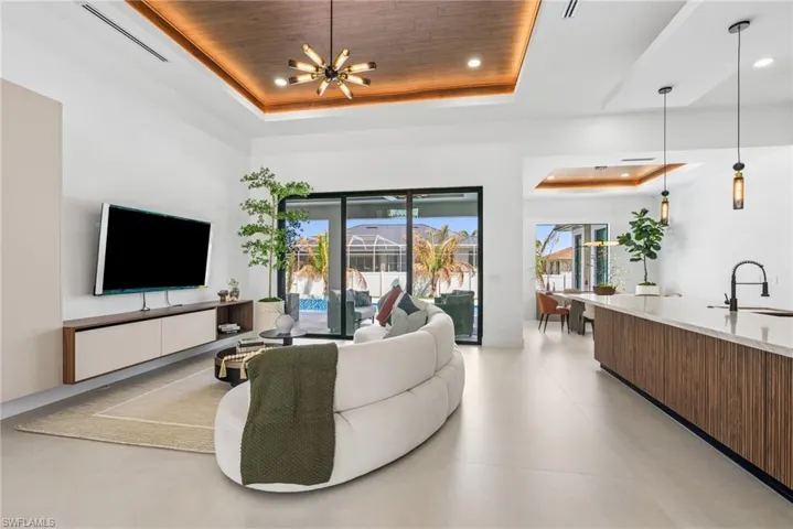 Spacious living area featuring a wood-finish tray ceiling with accent lighting, large format tile flooring, and sliding glass doors opening to a pool area