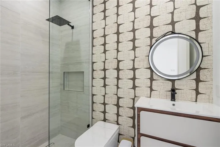 Bathroom featuring a glass-enclosed shower with a black rain showerhead, a built-in shower niche, a floating vanity with a white basin and matte black faucet, and an illuminated circular mirror