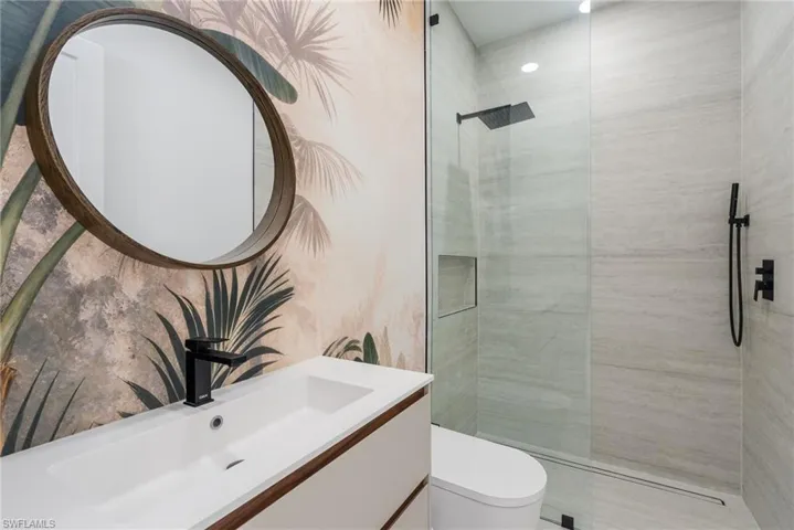 Contemporary bathroom featuring a floating vanity with an integrated sink, a circular wood-framed mirror, and a glass-enclosed shower with a recessed niche