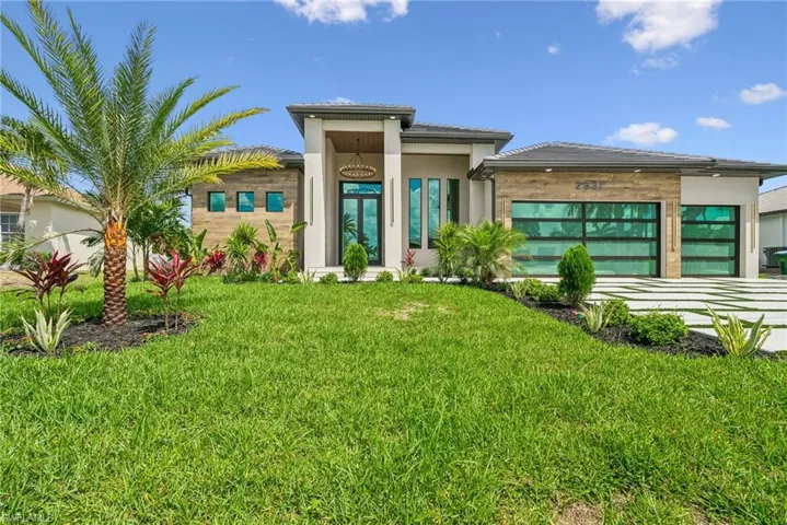 Contemporary exterior featuring a lush green lawn, mature palm tree, modern landscaping, segmented driveway, and two glass-paneled garage doors