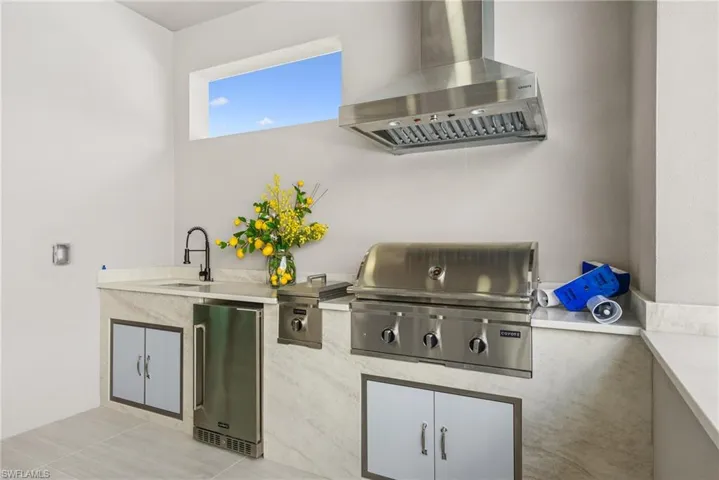 Outdoor kitchen featuring a stainless steel built-in grill, coordinating range hood, and integrated sink with a matte black faucet