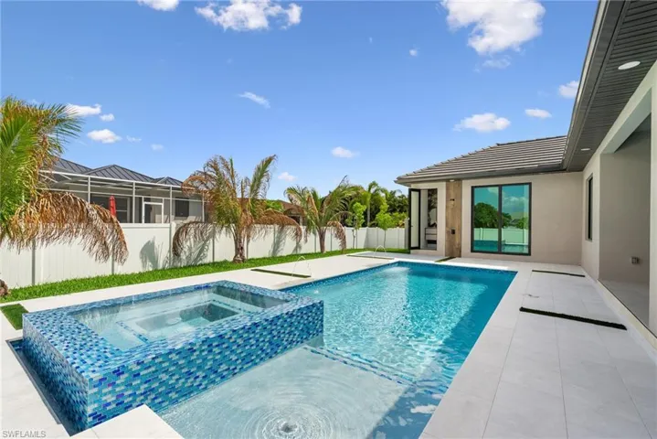 Outdoor living space featuring a rectangular pool with an integrated spa, mosaic tile detailing, a spacious white tiled deck, and multiple palm trees