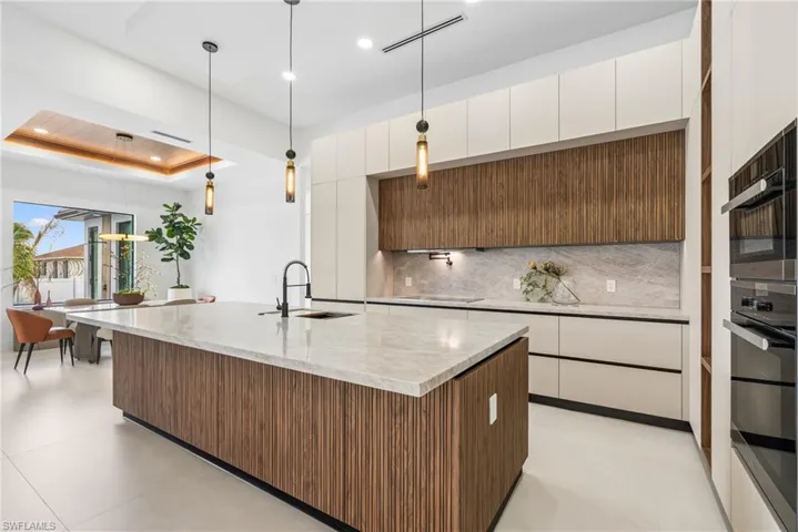 Spacious kitchen featuring a large island with a wood-finish base and light-toned countertop, integrated sink with a matte black faucet, contemporary pendant lighting, and a combination of wood-finish and light-toned cabinetry
