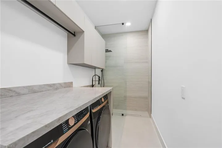 Laundry area featuring a stone countertop, built-in cabinetry, under-cabinet lighting, and a glass-enclosed shower with a rainfall showerhead
