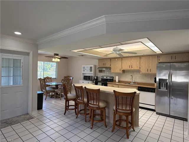 Kitchen featuring stainless steel appliances, decorative backsplash, a breakfast bar area, light tile patterned floors, and crown molding