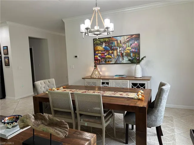Dining space with light tile patterned floors, crown molding, and a chandelier