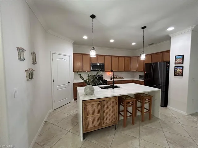 Kitchen with a breakfast bar area, brown cabinets, black appliances, light stone counters, and ornamental molding
