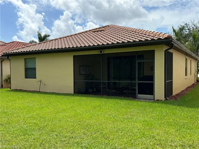 Back of property featuring a yard, stucco siding, a tiled roof, and a sunroom