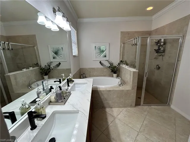 Bathroom with ornamental molding, a bath, a shower stall, double vanity, and light tile patterned floors