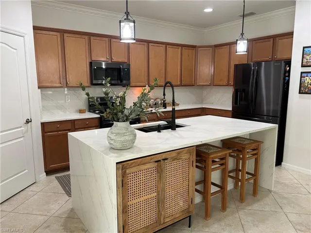 Kitchen featuring brown cabinetry, decorative backsplash, ornamental molding, light stone countertops, and black appliances