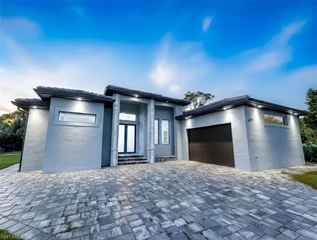 Prairie-style house with a garage, stucco siding, and decorative driveway
