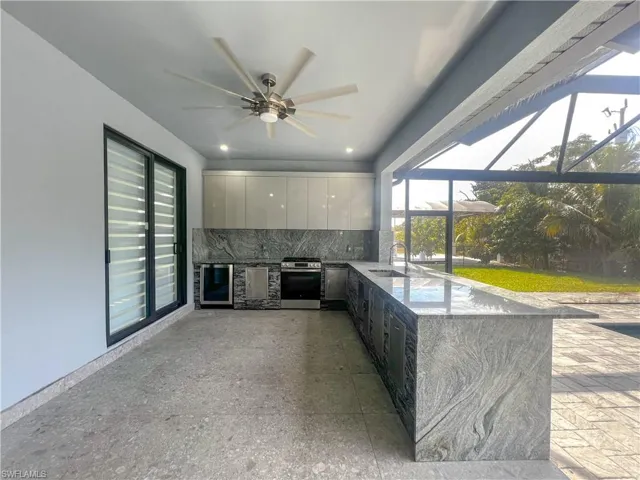 View of patio featuring exterior kitchen, a ceiling fan, a lanai, a sunroom, and wine cooler
