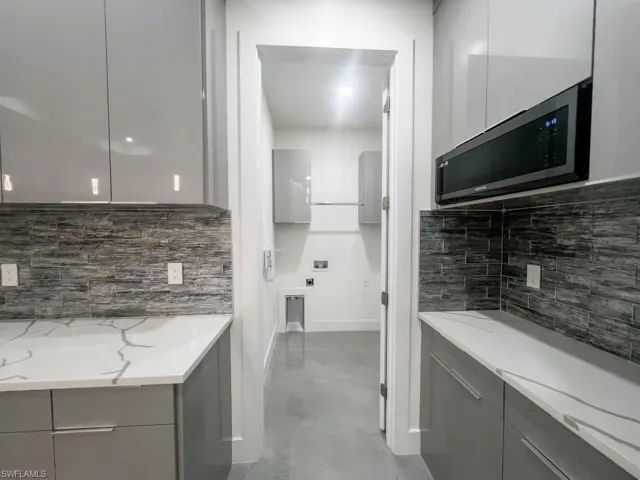 Kitchen featuring modern cabinets, gray cabinetry, stainless steel microwave, light stone countertops, and backsplash