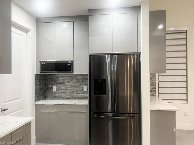 Kitchen featuring stainless steel appliances, modern cabinets, gray cabinetry, and light stone countertops