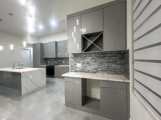 Kitchen with gray cabinets, light stone countertops, modern cabinets, pendant lighting, and decorative backsplash