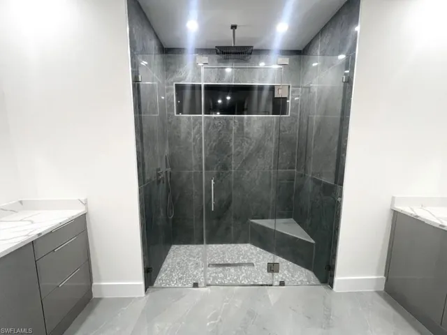 Full bathroom featuring vanity, a marble finish shower, and light marble finish floors