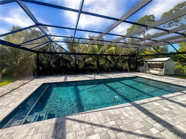 Outdoor pool featuring a sunroom, glass enclosure, and a storage shed