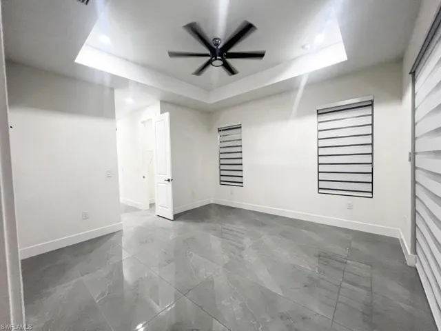 Unfurnished room with ceiling fan, a tray ceiling, and dark marble finish flooring