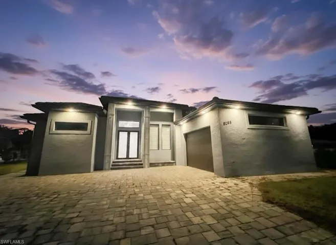 View of front of property with stucco siding, a garage, decorative driveway, and elevator