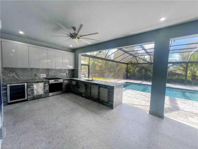 View of patio with an outdoor kitchen, ceiling fan, wine cooler, an outdoor pool, and a sunroom