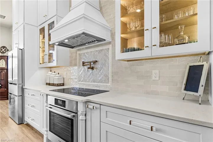 Kitchen featuring glass fronted cabinets, white cabinetry, stainless steel appliances, and light stone countertops