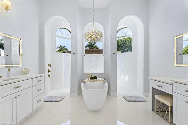 Primary Bathroom with two vanities, a freestanding bath, hanging lights, a walk in shower, and a high ceiling