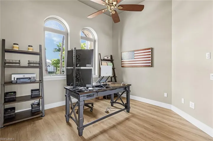 Office with light wood-style floors, a ceiling fan, and a high ceiling