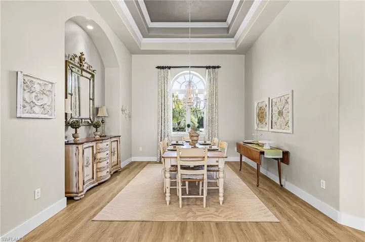 Dining room featuring light wood-style flooring, suspended lighting, ornamental molding, and a tray ceiling