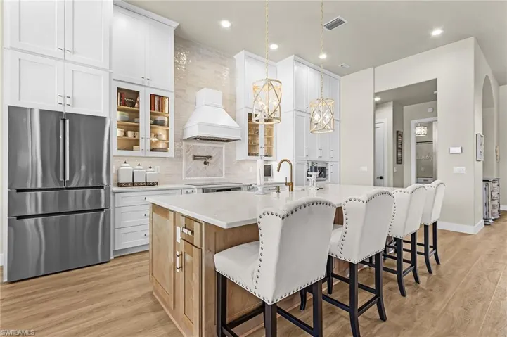Kitchen with freestanding refrigerator, a center island with sink, a kitchen breakfast bar, glass fronted cabinets, and dual tone cabinets