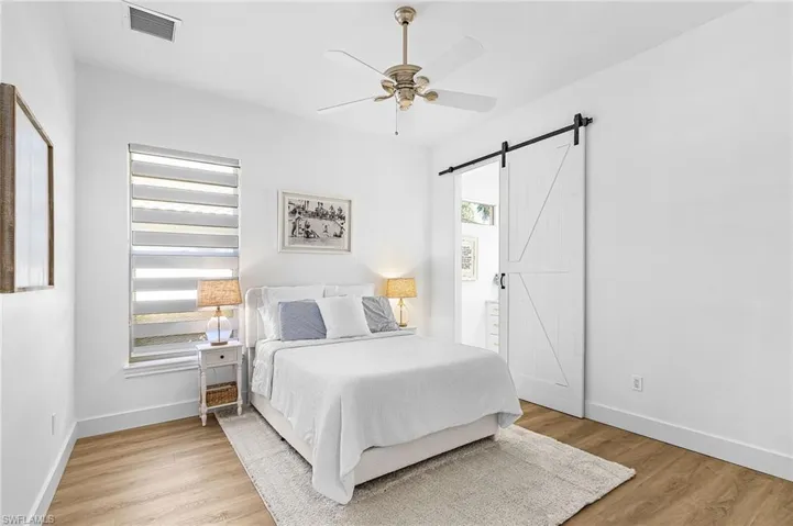 Bedroom with a barn door, light wood-type flooring, and ceiling fan
