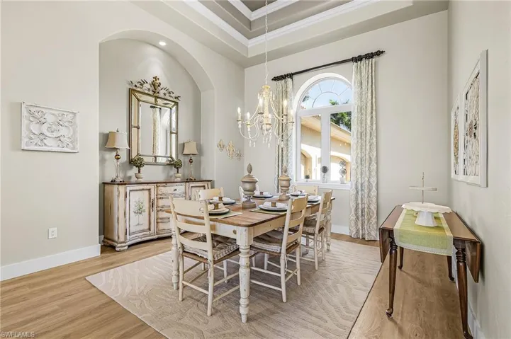 Dining area with hanging lights, light wood finished floors, ornamental molding, and a raised ceiling