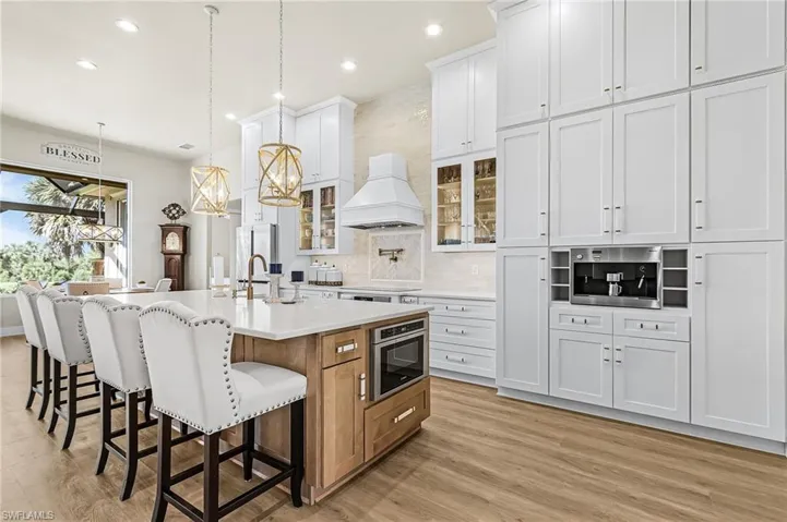 Kitchen with a kitchen bar, a large island, decorative backsplash, glass fronted cabinets, and hanging light fixtures