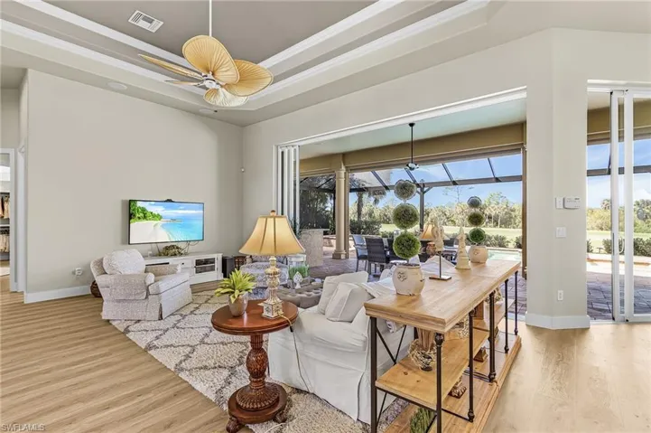 Living room with a sunroom, a raised ceiling, light wood finished floors, ceiling fan, and ornamental molding