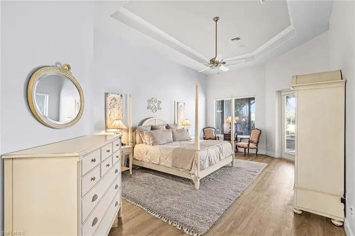 Primary Bedroom with access to exterior, light wood-type flooring, a raised ceiling, and a ceiling fan