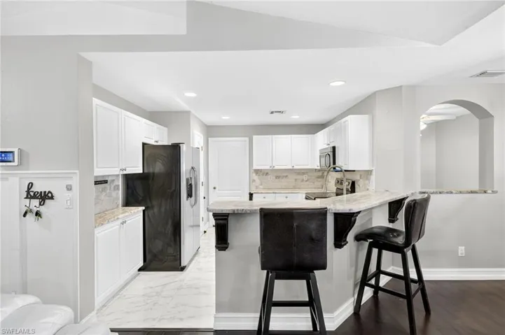 Kitchen featuring decorative backsplash, white cabinets, appliances with stainless steel finishes, a kitchen bar, and recessed lighting