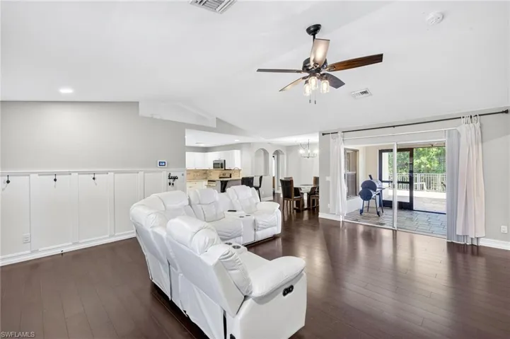 Living room featuring lofted ceiling, dark wood-style flooring, a ceiling fan, a chandelier, and arched walkways