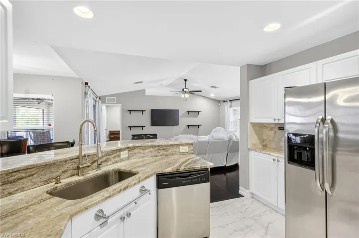 Kitchen with stainless steel appliances, white cabinets, light stone counters, open floor plan, and recessed lighting