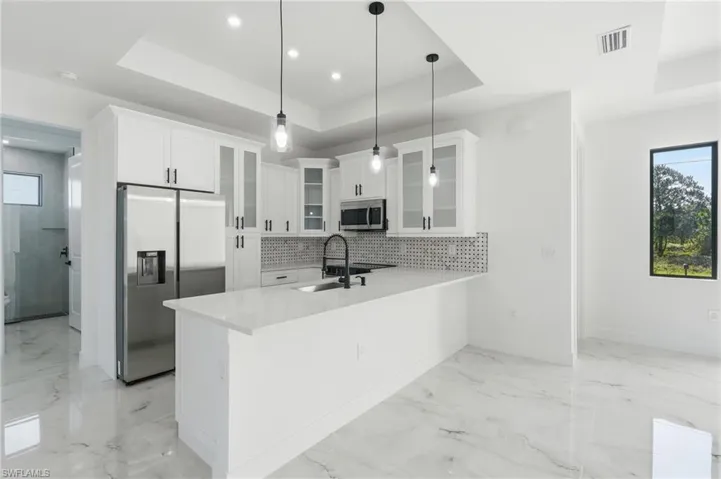 Kitchen featuring white cabinetry, a large kitchen island with a white countertop, stainless steel appliances, a mosaic tile backsplash, and recessed and pendant lighting
