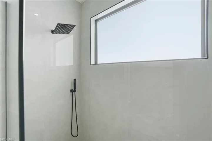 Shower with a matte black rain head fixture, coordinating hand-held shower, and light-toned tile surround