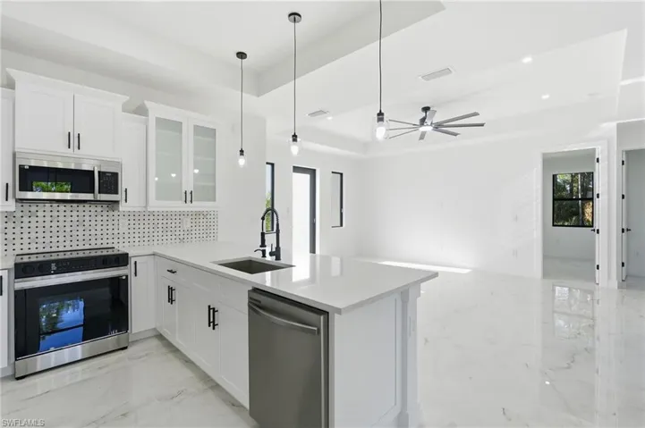 Kitchen featuring white cabinetry, stainless steel appliances, a center island with sink, and white tile flooring