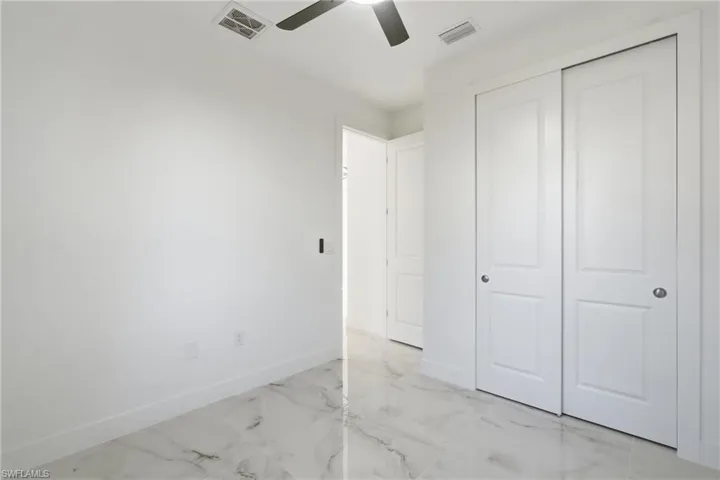 White walls, ceiling fan, white sliding closet doors, and marble-look flooring