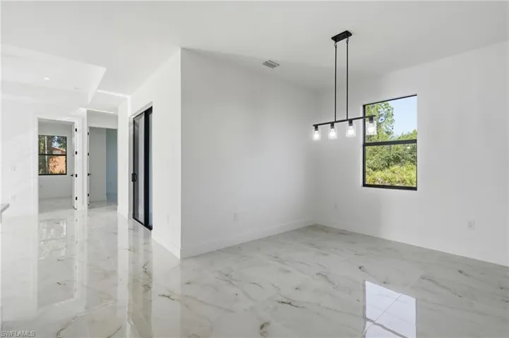 Bright, open dining space featuring polished stone-finish flooring, clean white walls, and a contemporary pendant light fixture suspended from the ceiling