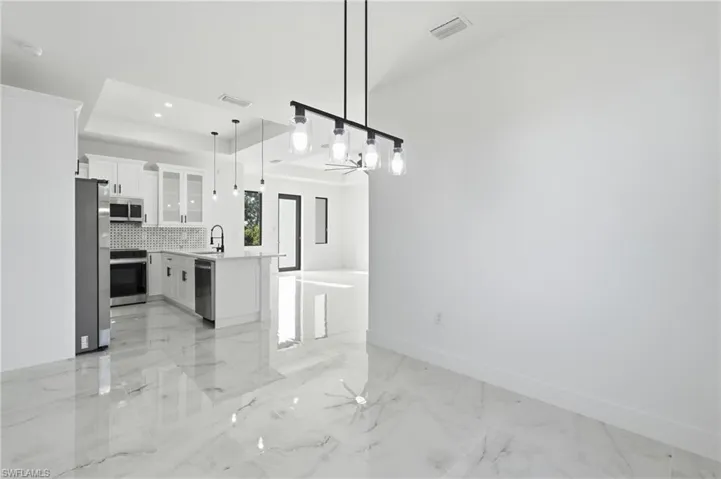 Open-concept living space featuring high ceilings, large format porcelain tile flooring, a kitchen island with seating, a patterned tile backsplash, and stainless steel appliances
