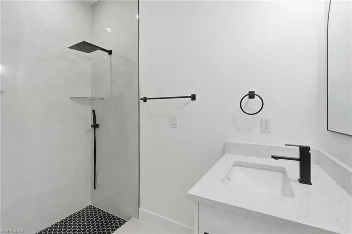 Glass-enclosed shower with a matte black rain shower head and handheld sprayer