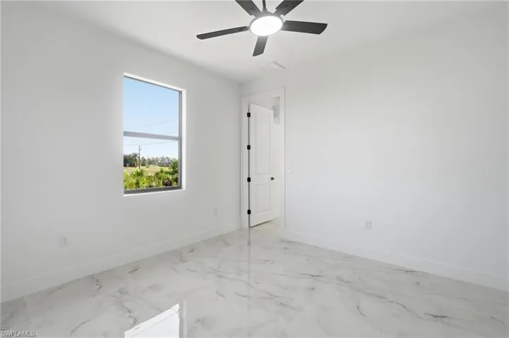 Clean white walls, modern ceiling fan with integrated lighting, and a white interior door with black hardware