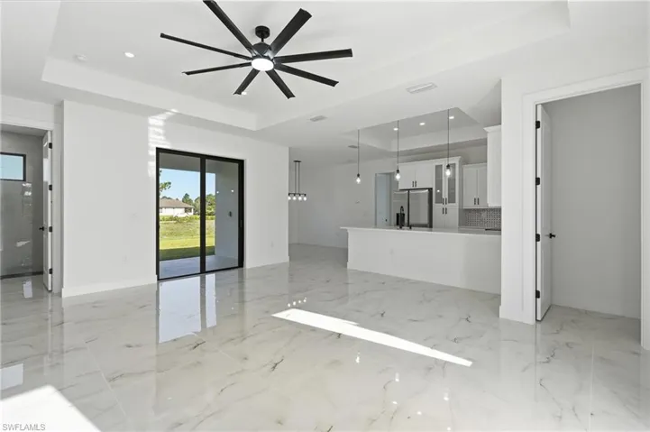 Glossy tile flooring, tray ceiling, modern ceiling fan, sliding glass doors, and a kitchen island with pendant lighting