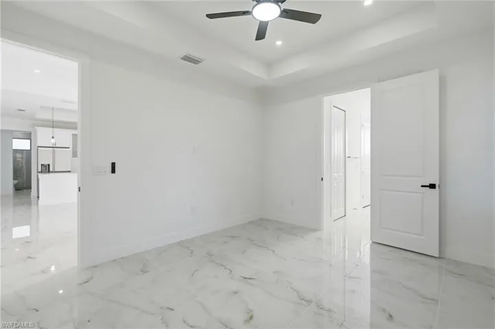White walls, tray ceiling, recessed lighting, ceiling fan, and large format polished tile flooring